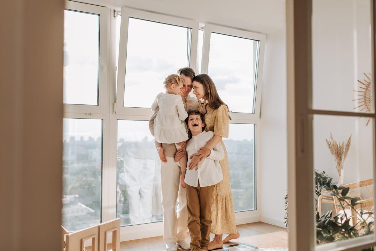 A loving family embraces near a large window in a bright, airy room, exuding warmth and togetherness.